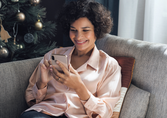 Woman sitting on sofa looking at phone with christmas tree in background