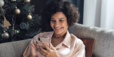Woman sitting on sofa looking at phone with christmas tree in background