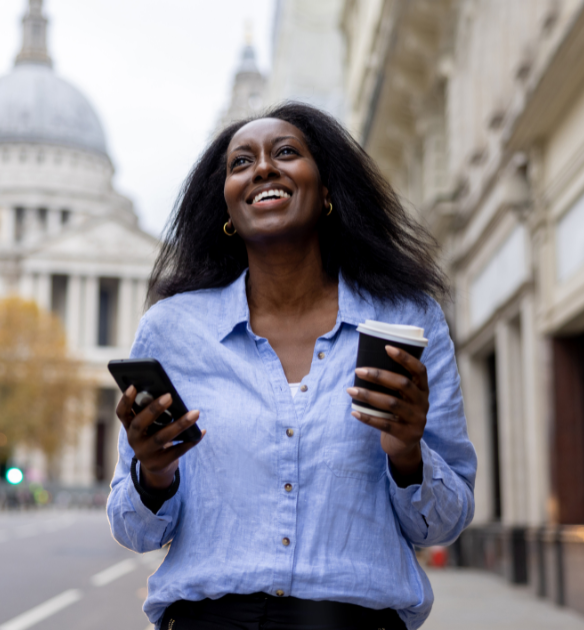 woman smiles into the sky while holding phone and coffee