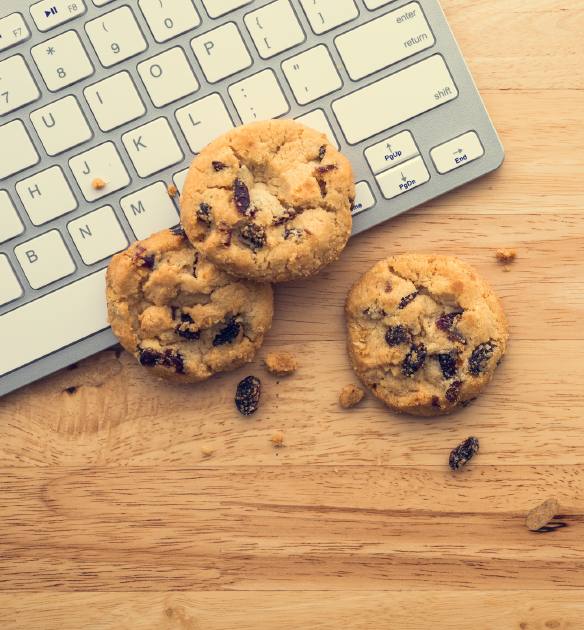 Three chocolate chop cookies scattered over a white apple keyboard on a wooden desk