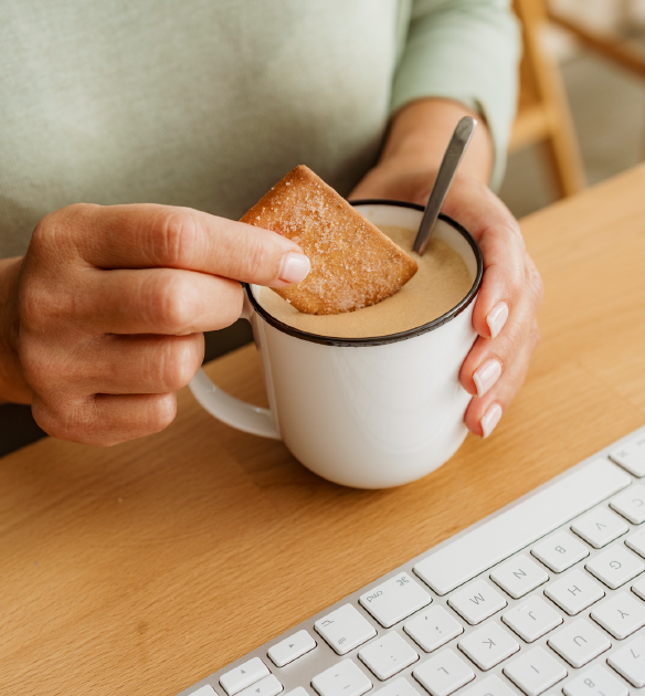 White person sits at a computer desk, dunking a shortbread cookie into a cup of English breakfast tea