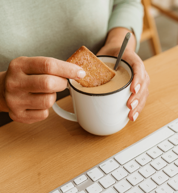 White person sits at a computer desk, dunking a shortbread cookie into a cup of English breakfast tea