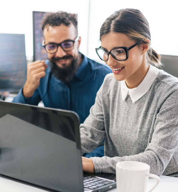 Millennial woman with black glasses and a grey sweater looks at a black laptop with a Gen X man with black glasses in a blue sweater. They're reading about future-focused affiliate tracking.